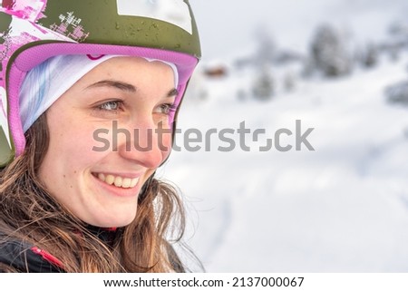 Woman with brown hair, wearing a ski helmet smiling while looking to the right side of the picture, snow landscape copyspace, close-up, horizontal