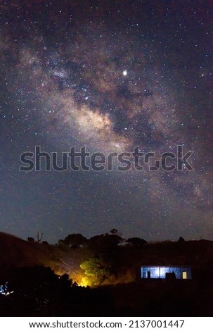 Magnificent Milky way Galaxy photo on a blue dark sky with bonfire and a small house in the foreground.