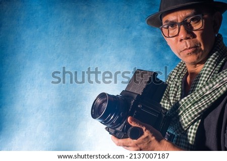 photographer holding medium format camera. Professional photographer portrait in studio blue background.