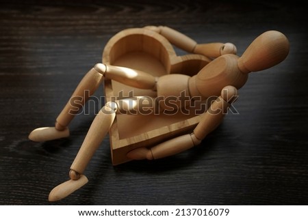 wooden model of one human ( man or woman) sitting in deep  heart shaped box. Empty space for your text. black wood table surface