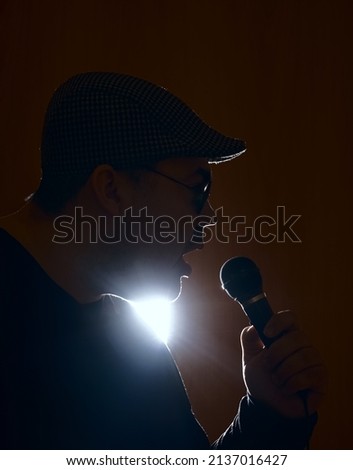 Portrait of attractive talented man singing in microphone hit rock roll isolated over shine yellow color background. checkered cap and round sunglasses.
