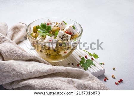 Tasty green olives with Feta cheese, pepper and fresh parsley in glass bowl with oil on grey concrete background