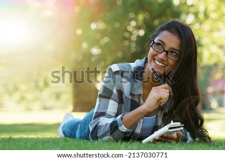 Jotting down her thoughts. A young woman lying on the grass writing in a notebook.