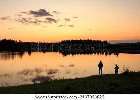 Sunset on the lake and silhouettes of people, against the background of the forest, summer, orange sky.