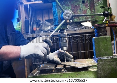 Employee drilling aluminium flat steel plate with bench drill. Metal Drill bit makes holes in Steel billet on industrial machine. Metal work industry