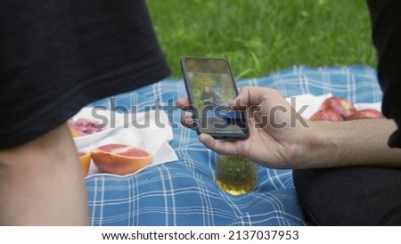 A man's hand holds a phone and flips through photos in nature in the summer. LGBT