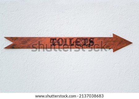 Wooden arrow sign pointing the direction of the toilets at a restaurant.