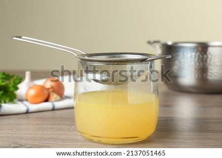Straining delicious broth through sieve on wooden table