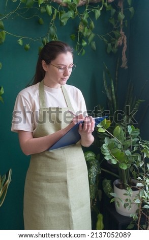 Young adult entrepreneur with tablet. Florist owner of a flower shop. The concept of retail and wholesale sales. The seller counts the goods in uniform