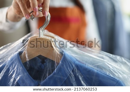 Worker giving to client clean clothes hanging on hangers at dry cleaning company Royalty-Free Stock Photo #2137060253