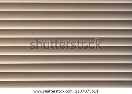 Closed window blinds illuminated by the sun, background texture.