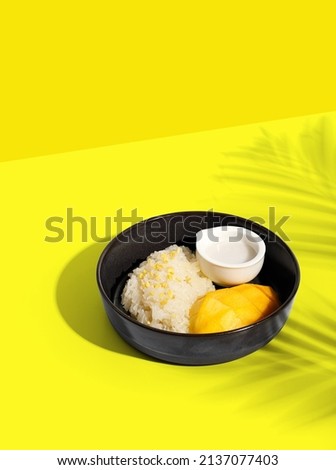 Thai Mango Sticky Rice, Southeast Asian dessert in black plate on yellow background with palm leaf shadow, clipping path. Royalty-Free Stock Photo #2137077403