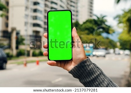 Girl on the street holding smartphone with Green screen waiting for car to arrive. Chroma Key.