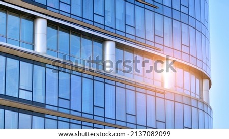 Minimalist glass facade, steel framework holding the large transparent panels. Contemporary commercial architecture, vertical converging geometric lines. Blue sky reflection in the glass panels