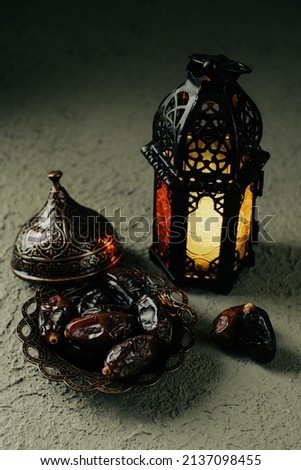 An illuminated Moroccan decorative lamp and dates in an old, antique plate. Ramadan background concept