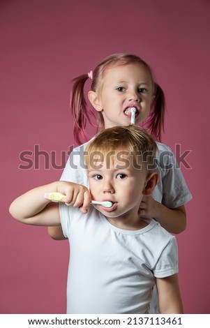 Smiling caucasian little boy and girl cleaning his teeth with electric sonic and manual toothbrush on pink background.