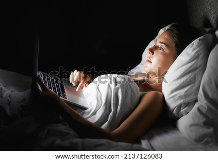 Just one more episode.... A pretty brunette browsing on her laptop while lying in bed. Royalty-Free Stock Photo #2137126083