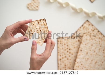 Woman's hand holds Matzah shape of house. Traditional of Jewish Holiday on Passover. Home symbol of lovely family. top view, layout. real estate agency Royalty-Free Stock Photo #2137127849
