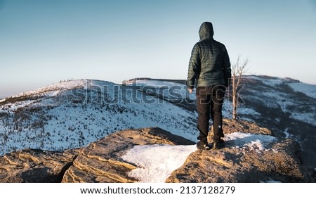 the man stands on top of the mountain and looks away. A photo showing mountain climbing or the concept of achieving goals and achieving achievements