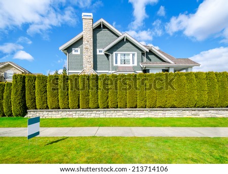 Beautiful house behind green hedge fence with empty for sale, lease, rent sign. Landscape trimming design.