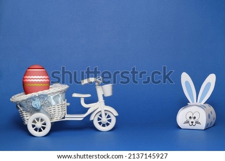 Blue easter bunny and an easter egg on the toy bicycle with blue background.