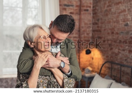 hug between caucasian elderly mother and her middle-aged bearded son medium shot. High quality photo Royalty-Free Stock Photo #2137180315