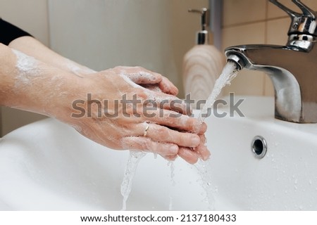 Two female hands with soapy foam in a stream of tap water in the bathroom close-up. The concept of hygiene, cleanliness and protection against coronavirus COVID-19.
