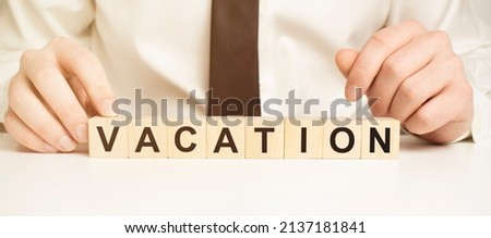 Wooden cubes with letters on a white table. The word is VACATION. White background with photo frame, house plant.