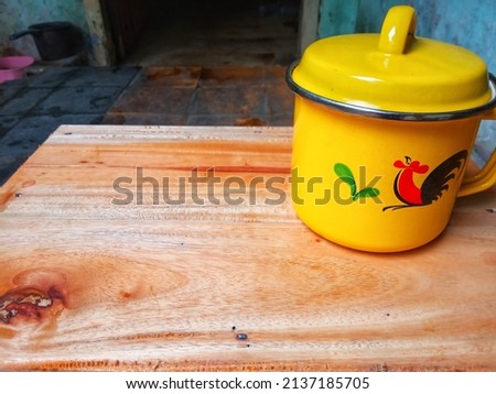 A yellow tea cup with a picture of a rooster placed on a small brown table
