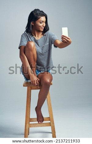 Darling, youre different. Studio shot of a beautiful young woman taking a selfie while sitting on a wooden stool.