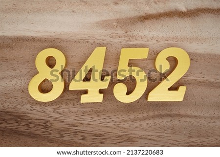 Wooden  numerals 8452 painted in gold on a dark brown and white patterned plank background.