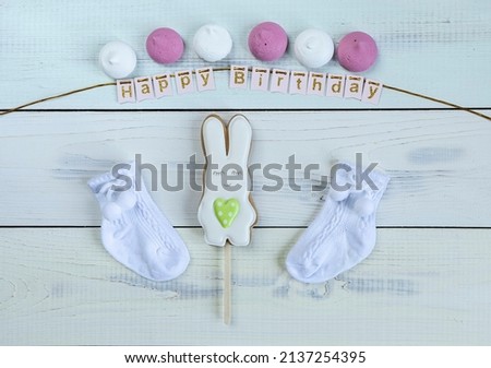 white and green gingerbread in form of Easter bunny, cute newborn booties, sweet marshmallows and Happy birthday lettering on light wooden background