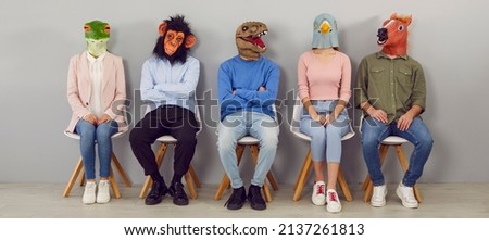 Diverse people in animal masks on head sit on chairs in line wait for interview or recruitment talk. Unknown job candidates in headmasks in queue indoors. Fun at workplace. Banner shot. Royalty-Free Stock Photo #2137261813