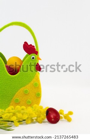 Felt rooster basket with painted eggs and mimosa flowers on white background. Easter. Copy space