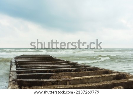 The base of an old concrete pier in the Black Sea. The stone base of the pier in the waves and foam in the ocean in cloudy weather. Destroyed pier on the beach in Magnetiti Ureki in Georgia Royalty-Free Stock Photo #2137269779