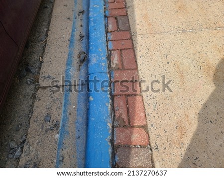 The side of a sidewalk with blue paint going along it indicating a handicap parking space on the street.