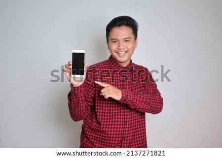 Portrait of attractive Asian man in casual plaid shirt showing and presenting blank screen mobile phone. Advertising concept. Isolated image on white background
