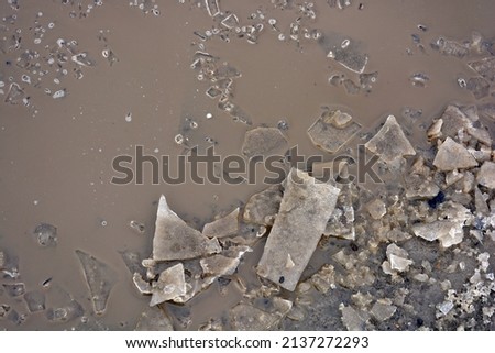 Broken transparent ice, small pieces of ice crust lie near a frozen puddle and float in the water. Spring is warming, the ice is melting on the street. 