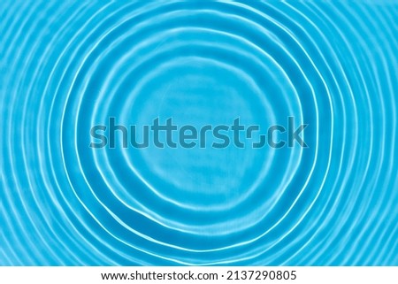 Wave from a drop of water on blue water under natural light. Top view, flat lay. 