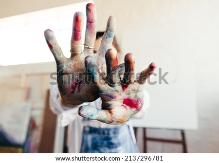 Painter blocking the camera from her face with her colour painted hands. Unrecognizable female artist standing in her art studio with her blank canvas in the background. Royalty-Free Stock Photo #2137296781