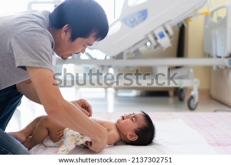 Asian daddy wipe the body of little son to reduce body temperature from fever in the hospital room, the concept of sickness child care by parent in the family in covid 19 pandemic. Royalty-Free Stock Photo #2137302751