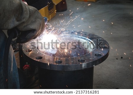 A welder is welding a flange assembly to a water pipe system. Royalty-Free Stock Photo #2137316281