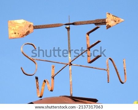 rusted metal homemade weather vane at the top of the roof with the blue sky background