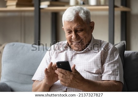 Happy elderly man look at cell phone screen rest on sofa at home, smiling enjoy received message with good news, read sms, share text messages spend leisure using modern wireless technology concept Royalty-Free Stock Photo #2137327827