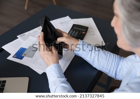 Senior woman sit at desk opening empty purse, no banknotes, without coins inside after pay bills and taxes, above top view. Financial crisis, bankruptcy, low pension of older citizen, poverty concept Royalty-Free Stock Photo #2137327845