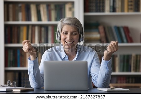 Happy middle-aged woman enjoy video conference sit at desk with laptop. Mature smiling female staring at computer having pleasant videoconference talk in office, watch videos spend leisure on internet Royalty-Free Stock Photo #2137327857