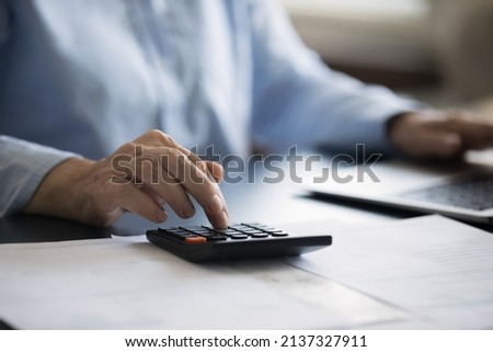 Close up cropped view woman sit at desk use calculator and laptop, calculates domestic expenditures, manage monthly finance, makes household bills payment through e-bank. Money saving, economy concept Royalty-Free Stock Photo #2137327911