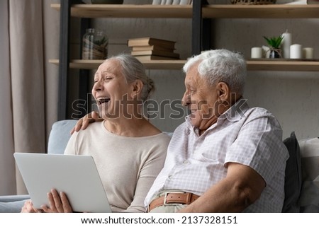 Happy mature couple spend time use laptop relax on sofa in living room, put computer on laps watch movie laughing enjoy comedy at home. Older generation and modern tech usage, leisure and fun concept