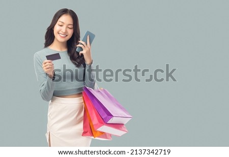 Young asian lady using mobile phone holding credit card carry shopping bags isolated over pastel green background and copy space Smiling young girl purchasing online through phone using credit card