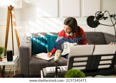 Composing new music. Talented young woman and musician writing a beautiful song while playing the electric guitar Royalty-Free Stock Photo #2137345471